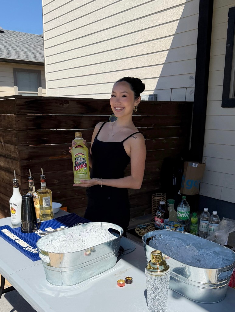 Smiling female Austin bartender holding Jose Cuervo margarita mix at a backyard party with ice buckets and bar setup
